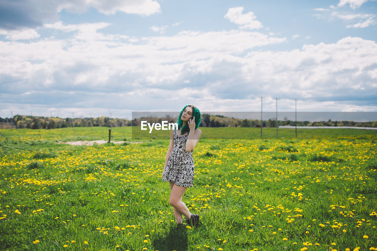 Full length of woman standing on yellow flowers field against cloudy sky