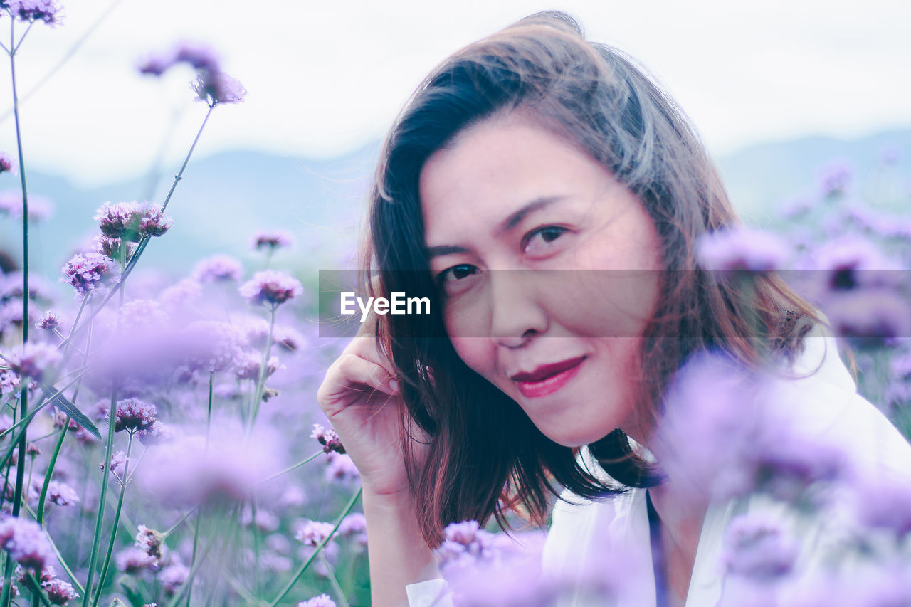 PORTRAIT OF SMILING YOUNG WOMAN WITH PURPLE FLOWERS