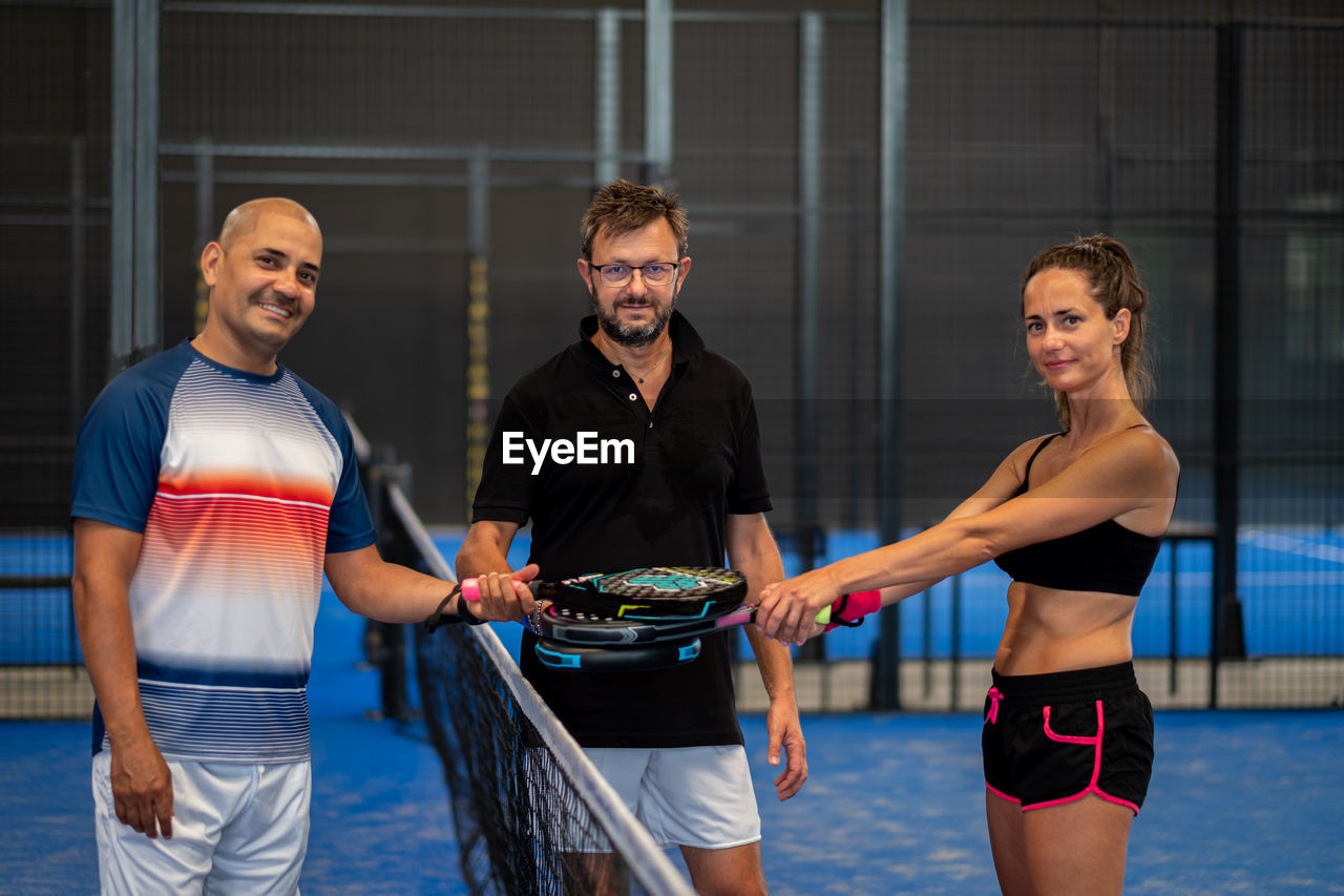 Portrait of smiling sportsman's posing indoor on padel court with rackets and balls