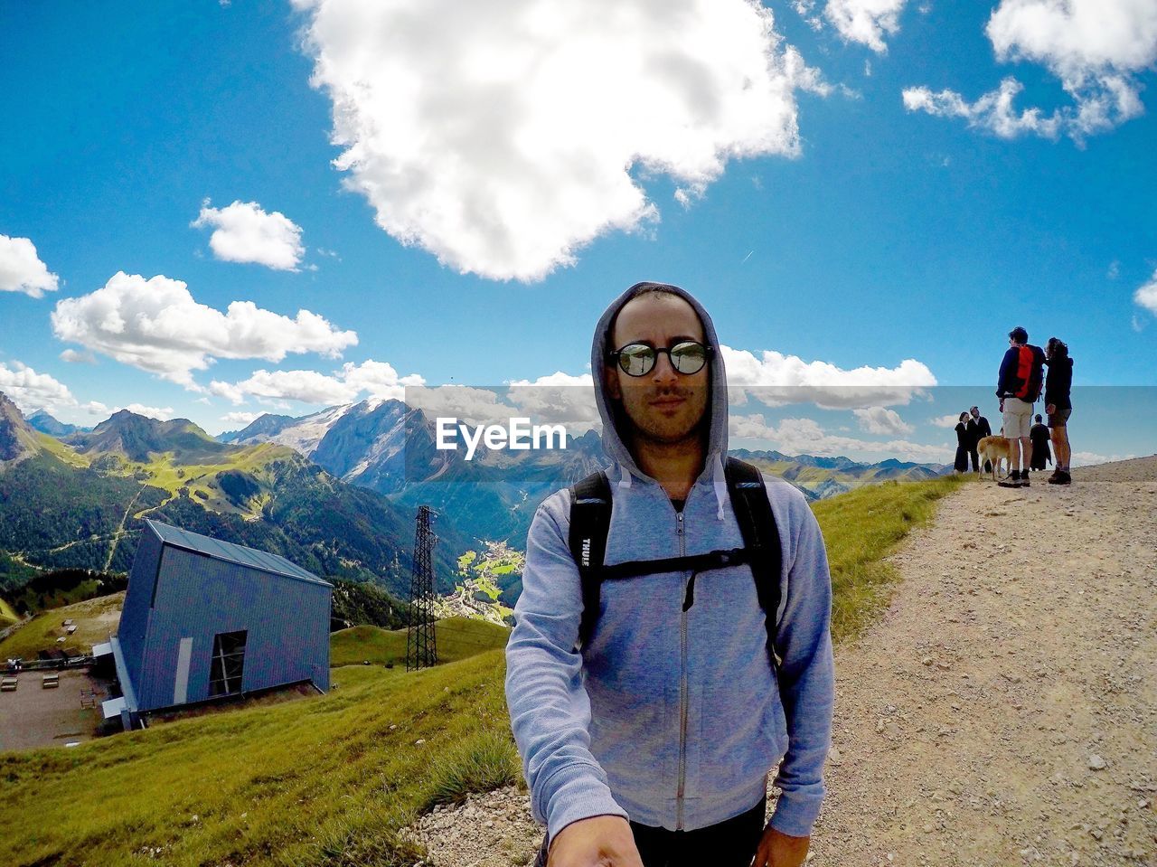 Portrait of young man wearing sunglasses standing on mountain against blue sky