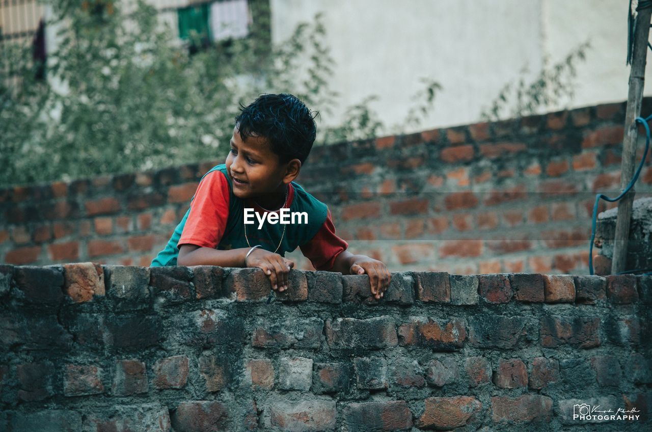 FULL LENGTH OF BOY PLAYING ON WALL AGAINST BRICK WALLS