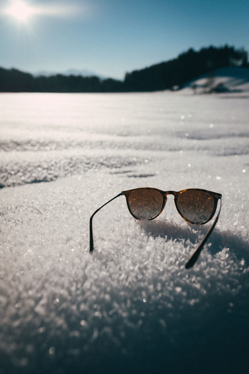 Close-up of sunglasses on snow against sky