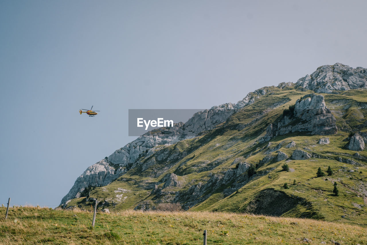 AIRPLANE FLYING ABOVE MOUNTAIN AGAINST CLEAR SKY