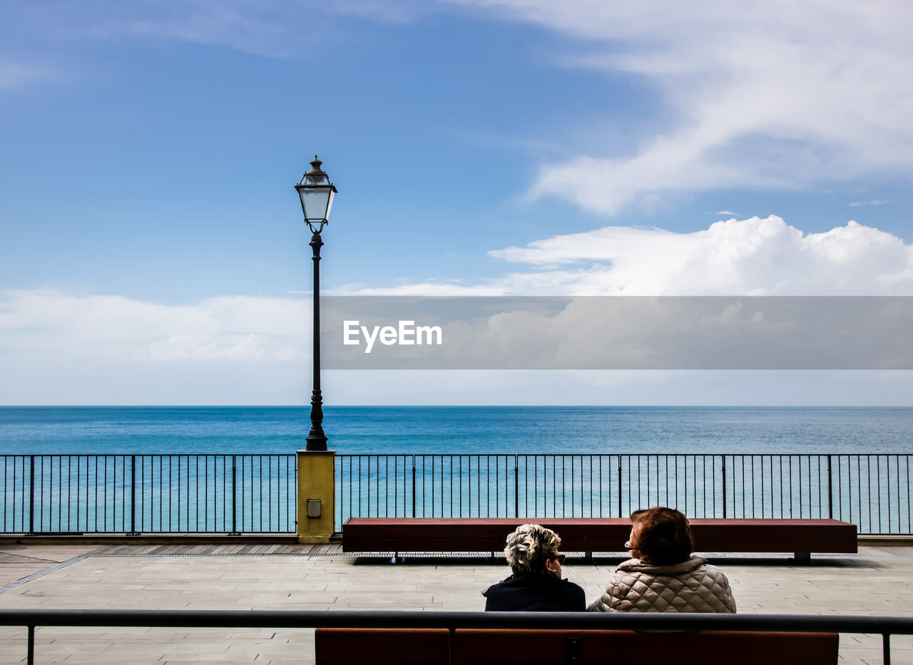 Rear view of mature couple sitting on bench against sea