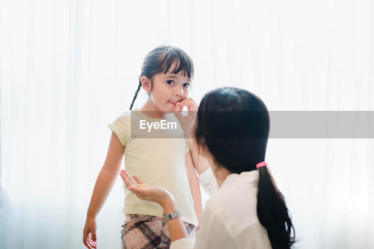 Young woman feeding food to daughter at home