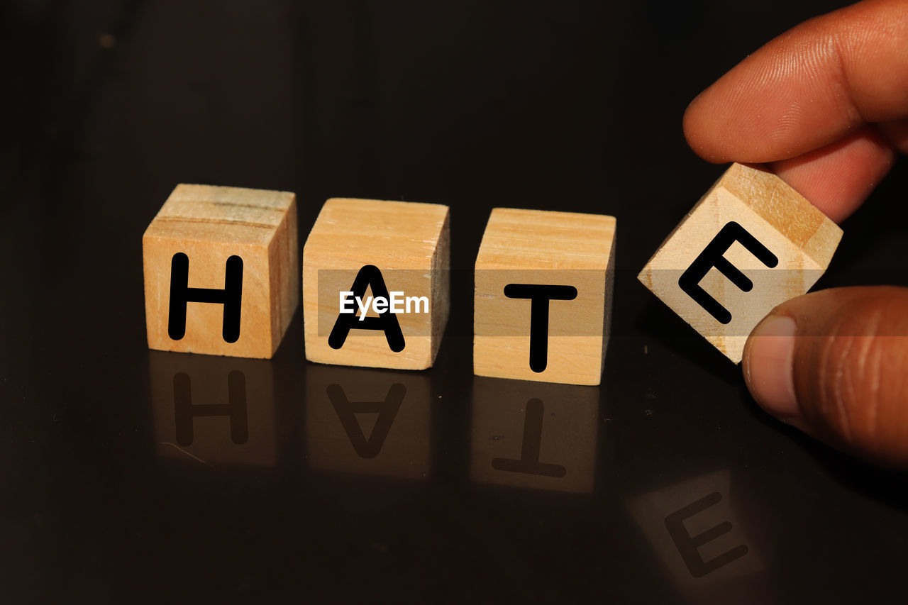 Cropped hand with hate text on toy blocks against black background