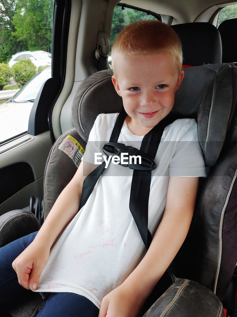 Cute boy sitting in his car seat, showing his juice stained t-shirt 