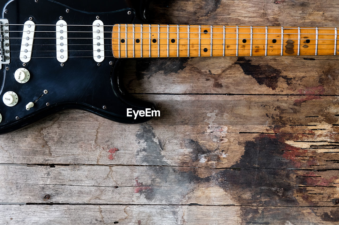 Detail of black electric guitar on a wood background.