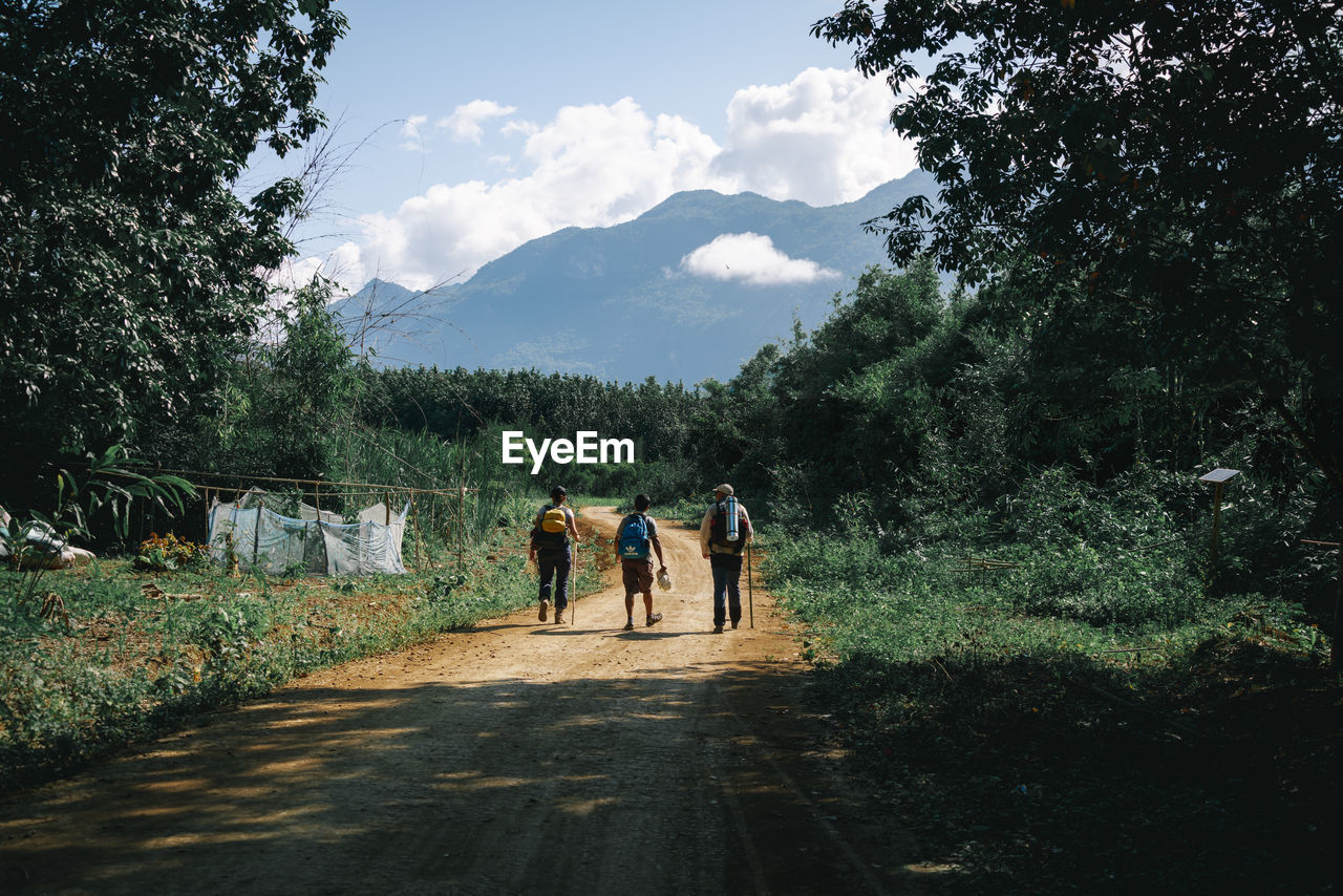 REAR VIEW OF PEOPLE WALKING ON ROAD AGAINST SKY