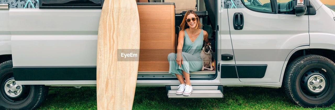 Woman sitting with her dog at the door of her camper van during a trip