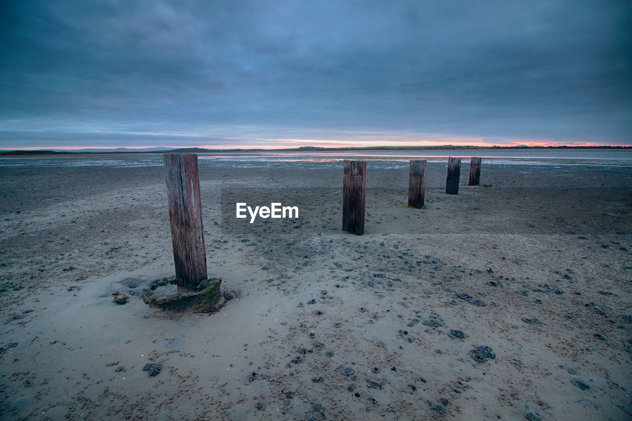 WOODEN POSTS ON BEACH AGAINST SKY