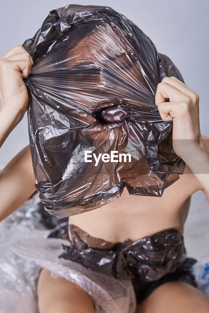 Young woman wearing plastic on face against white background