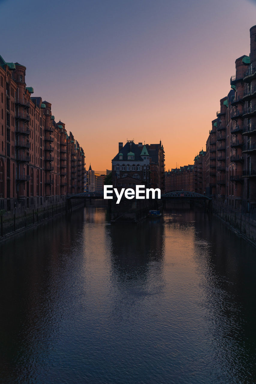 Buildings by river against sky during sunset at speicherstadt in hamburg