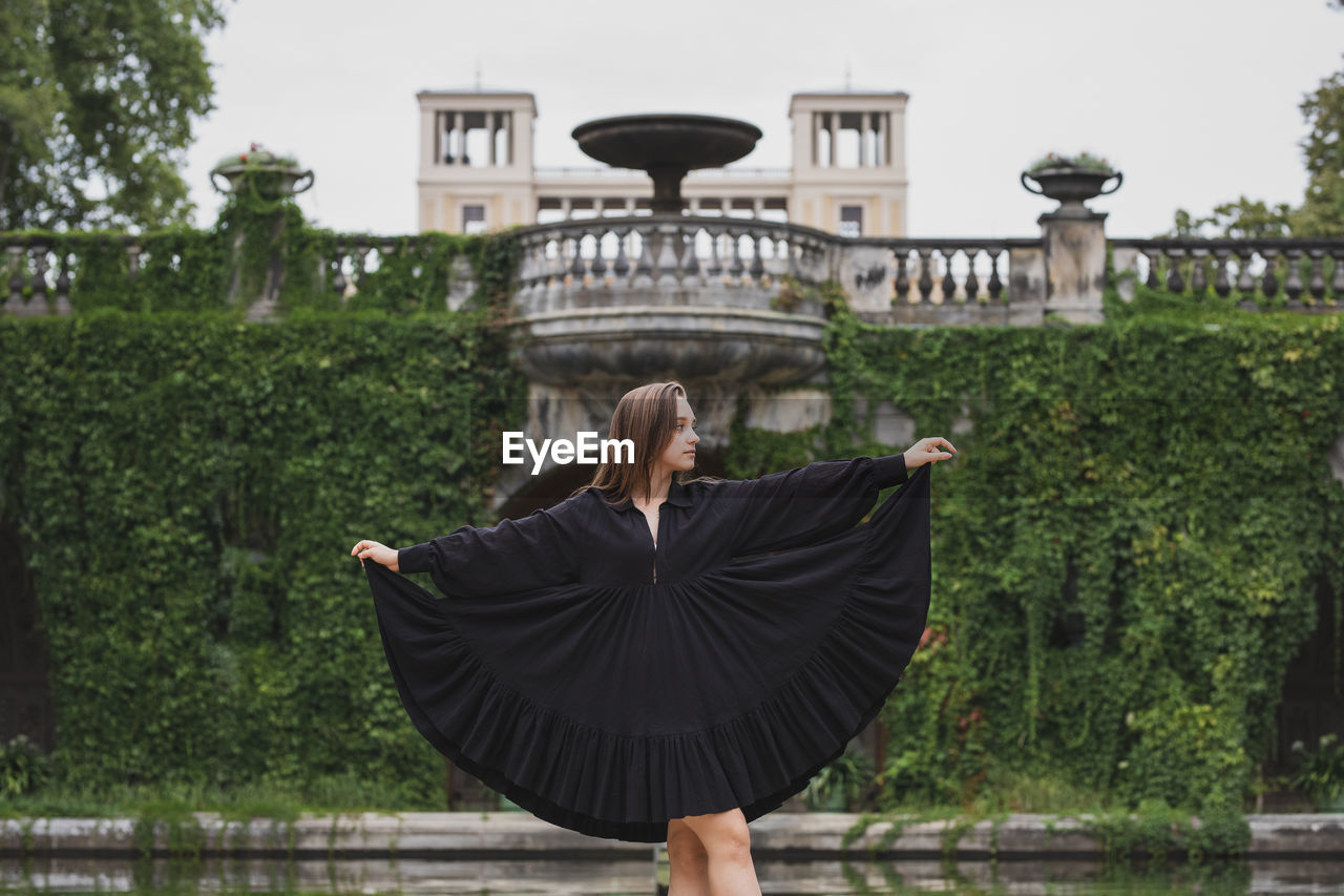 Young woman looking away while standing against built structure