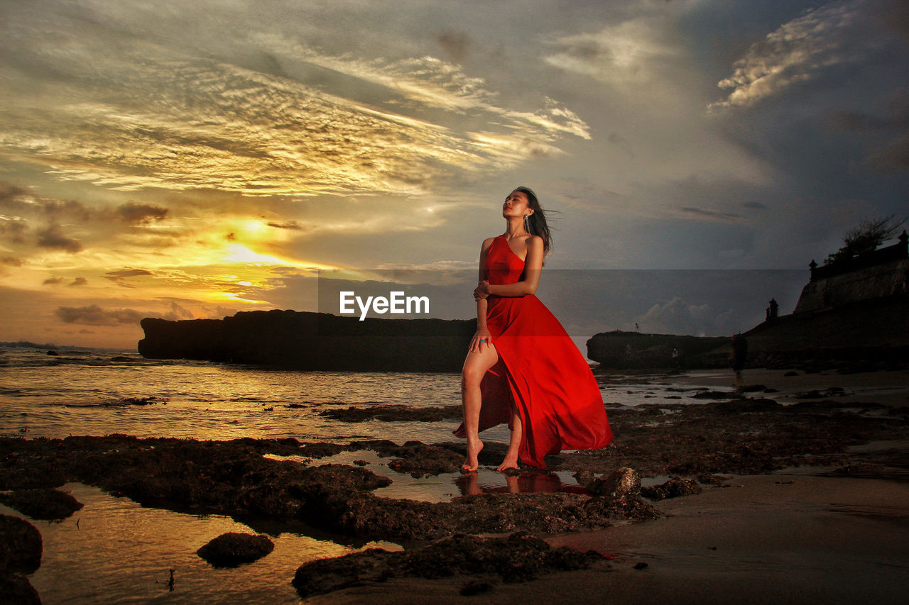 Rear view of woman standing at beach against sky during sunset