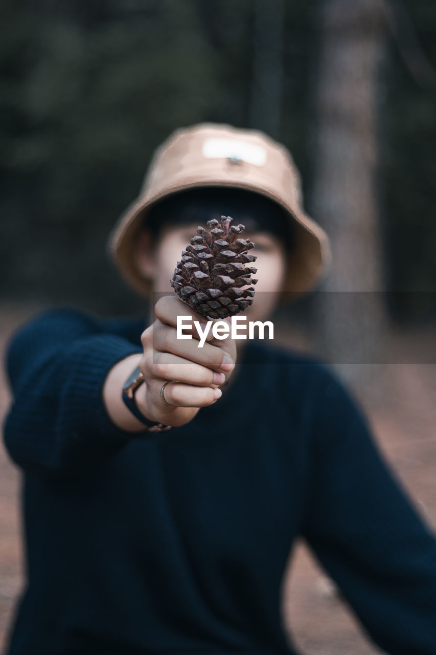 Close-up of man covering face with pine cone