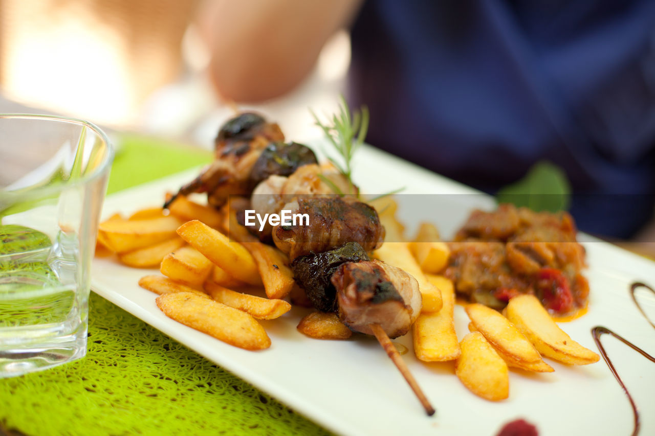 Close-up meat skewer with french fries and ratatouille on table