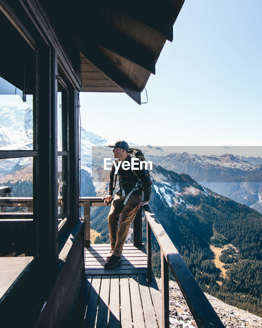 MAN STANDING ON RAILING AGAINST MOUNTAINS