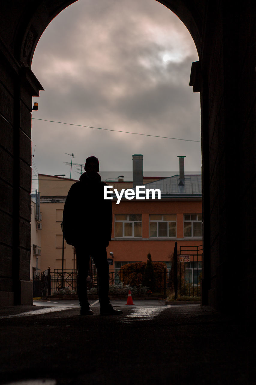 REAR VIEW OF SILHOUETTE MAN STANDING BY STREET AGAINST SKY