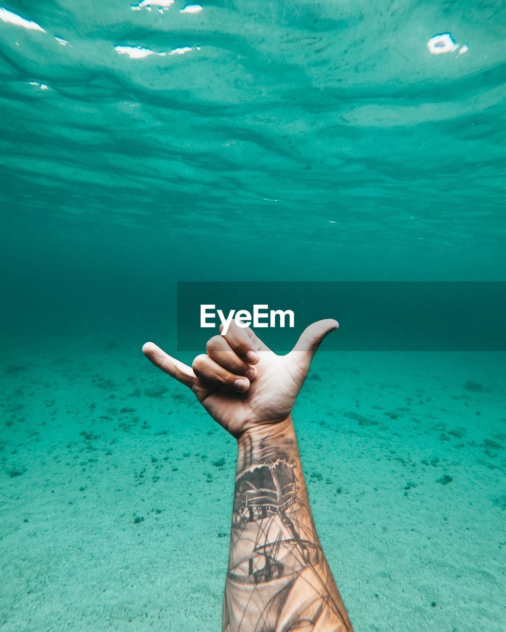 Cropped hand of man gesturing shaka sign in sea