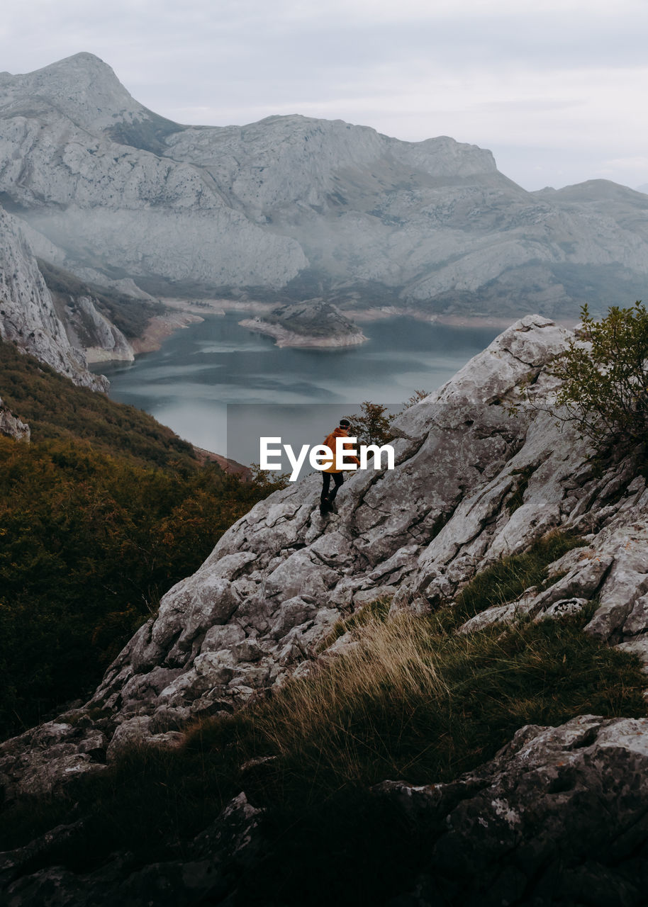 Man climbing on rock by mountains and lake