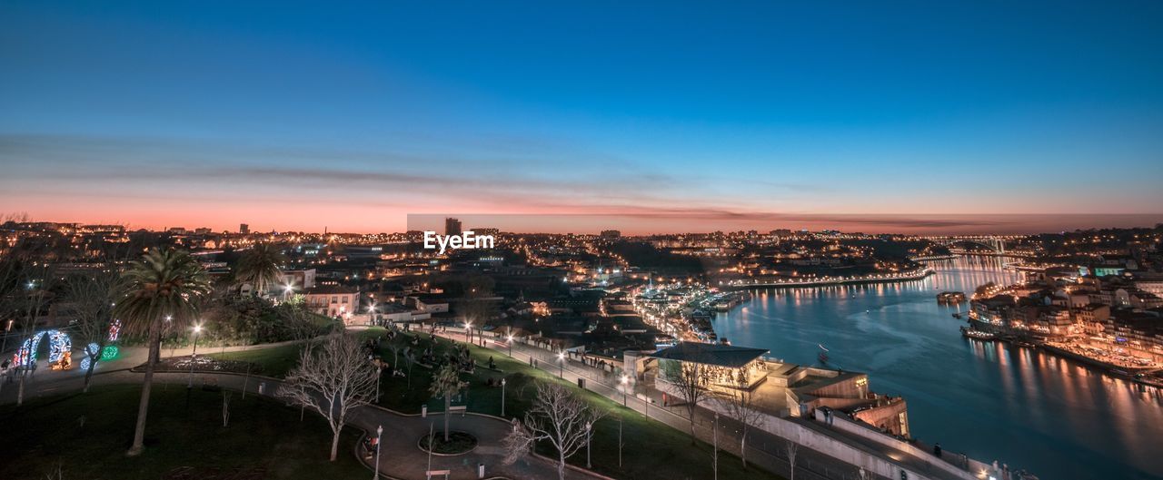 High angle view of illuminated buildings by river against sky