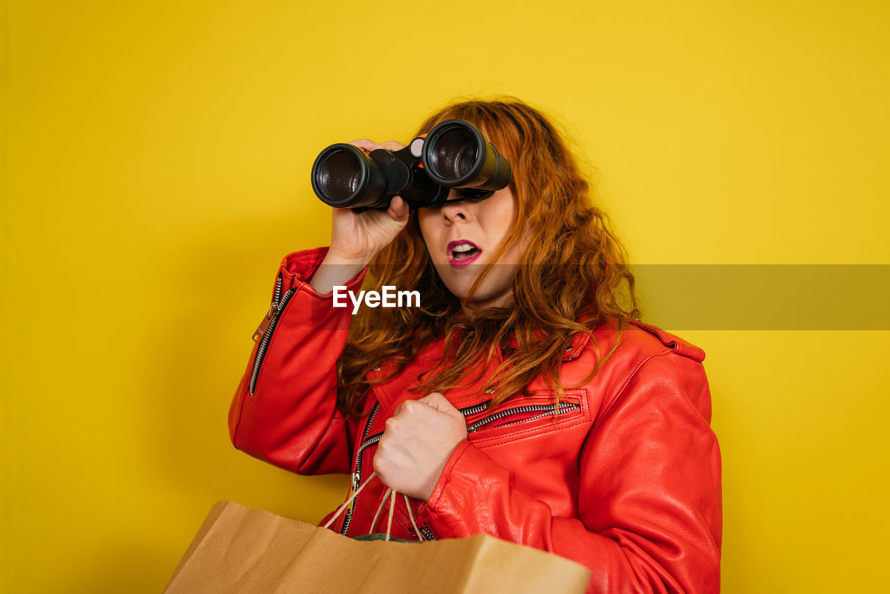 women, adult, colored background, yellow, fashion, young adult, one person, studio shot, red, portrait, photo shoot, indoors, yellow background, happiness, clothing, smiling, fun, emotion, hairstyle, copy space, costume, long hair, person, lifestyles, glasses, female, positive emotion, cheerful, holding, waist up, casual clothing, looking, bag, sunglasses, enjoyment