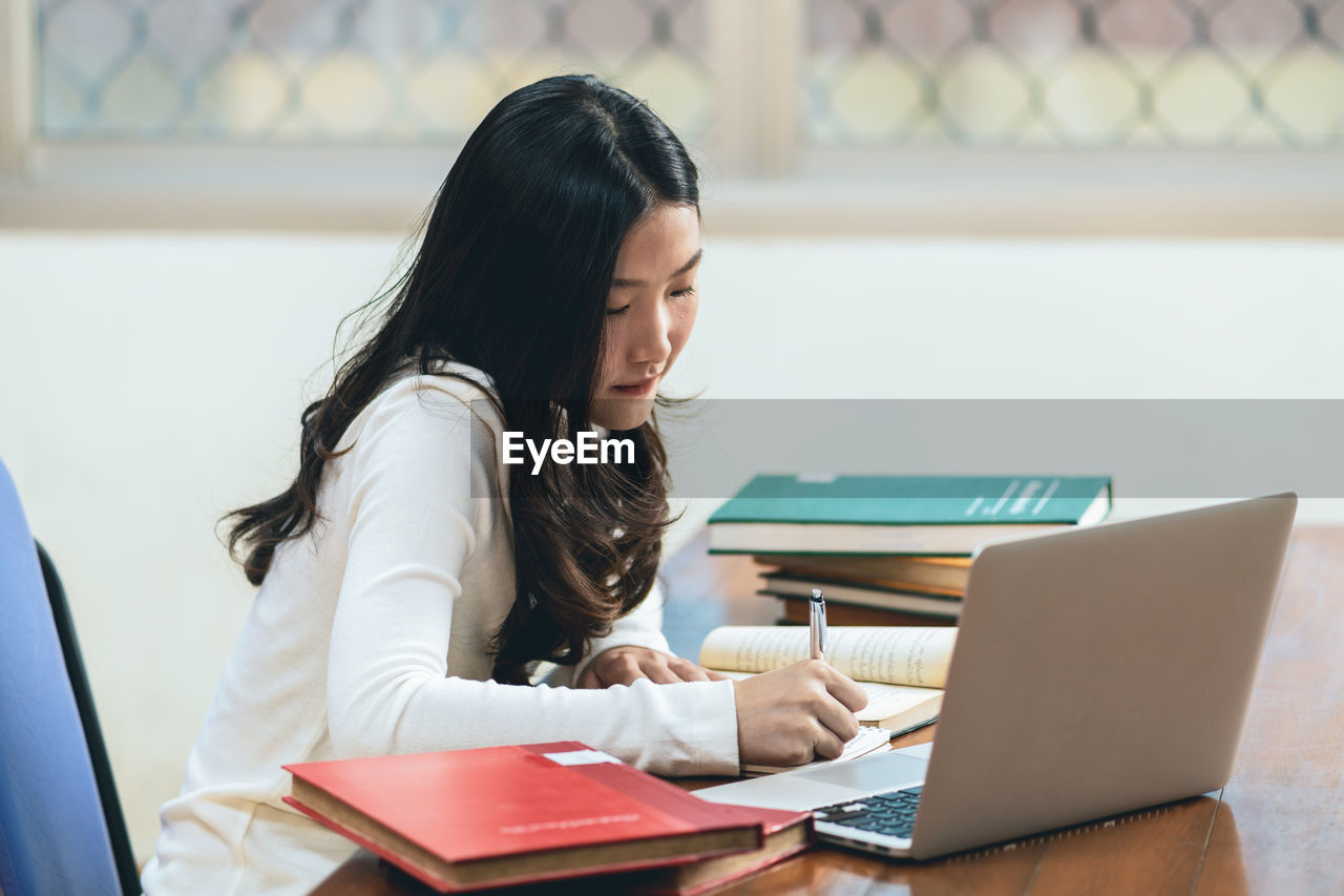 Woman writing in book while sitting at library