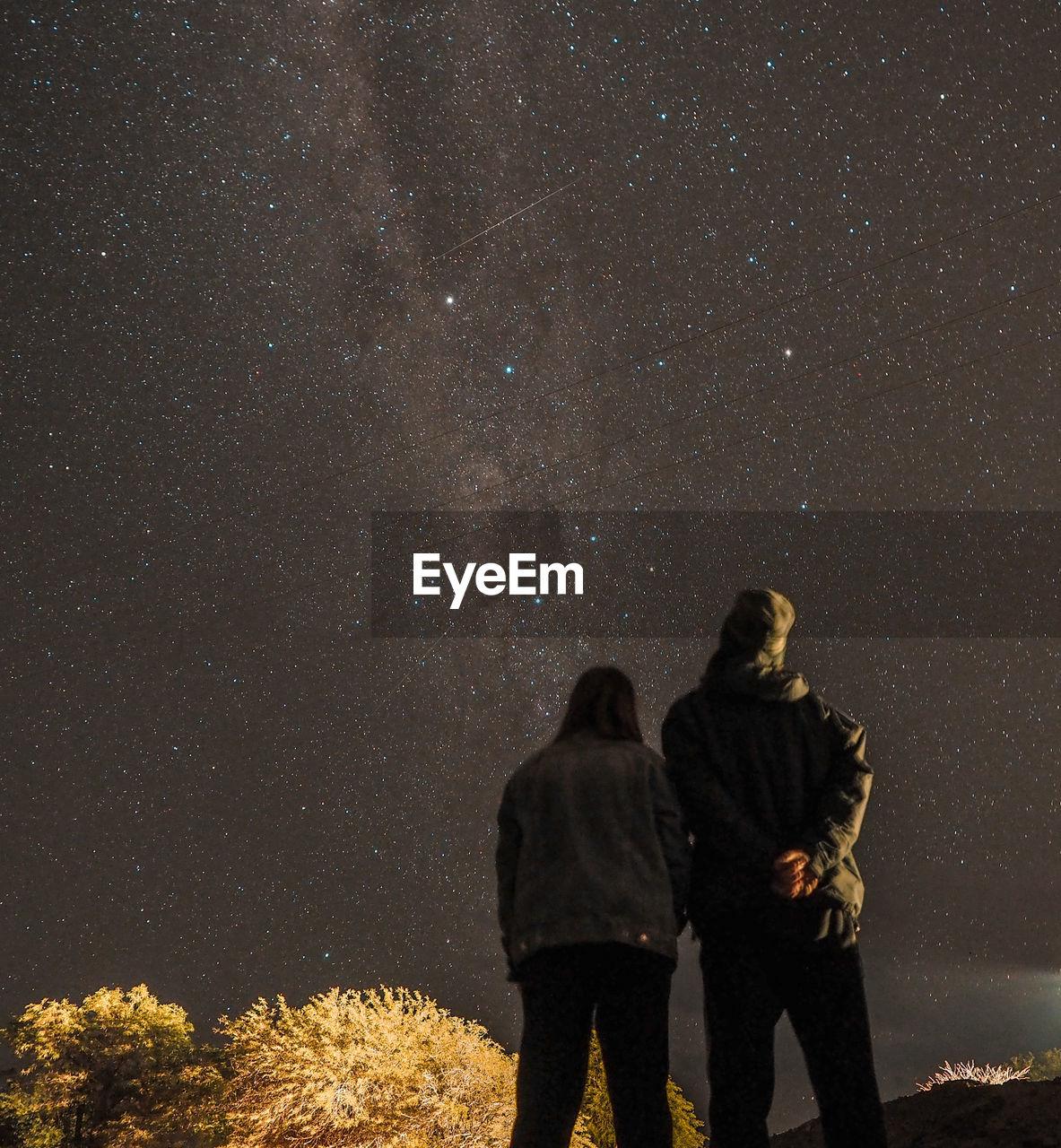 Rear view of couple standing on field against star field at night