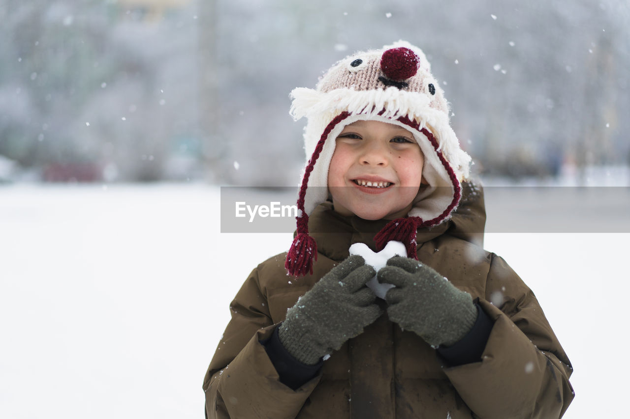 Child enjoying winter. the boy holds a heart made of snow in his hands in winter day. love concept.
