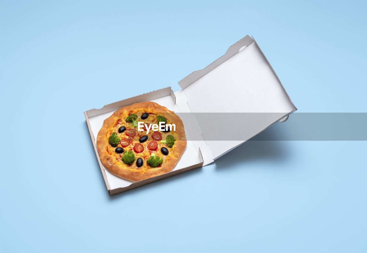 Top view of a vegan pizza in cardboard box on blue table. pizza box isolated on colored background. 