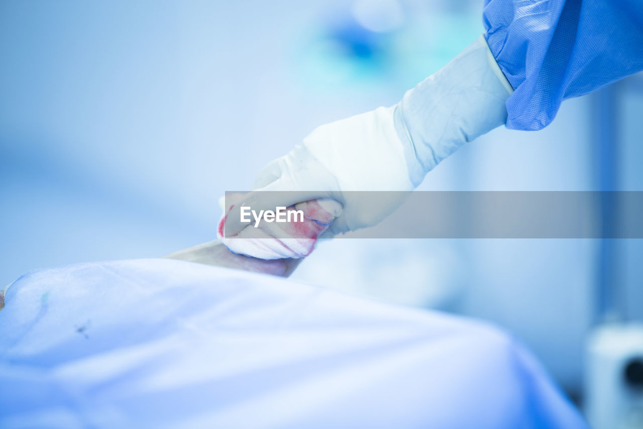 Cropped hand of surgeon wiping patient wound in operating room