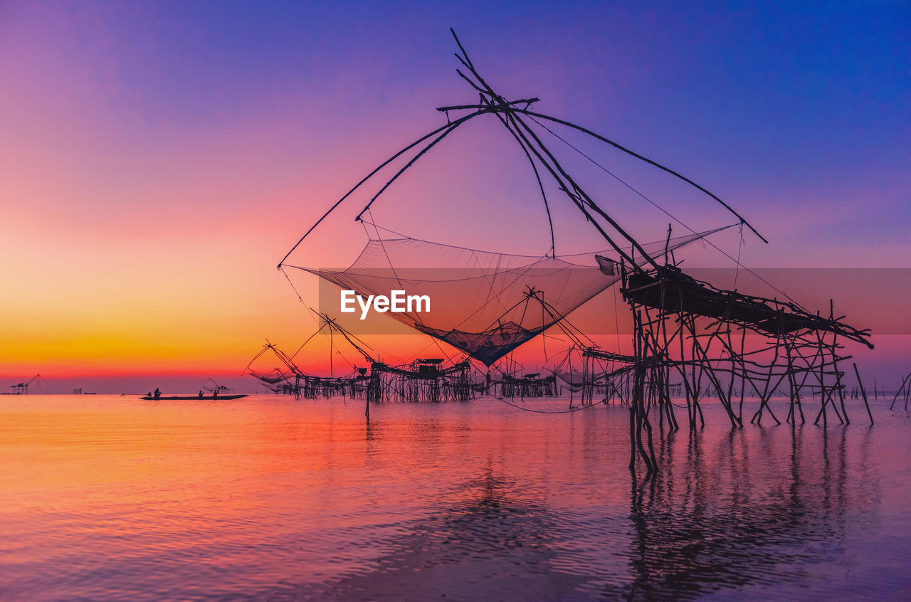 SILHOUETTE FISHING NET BY SEA AGAINST ORANGE SKY