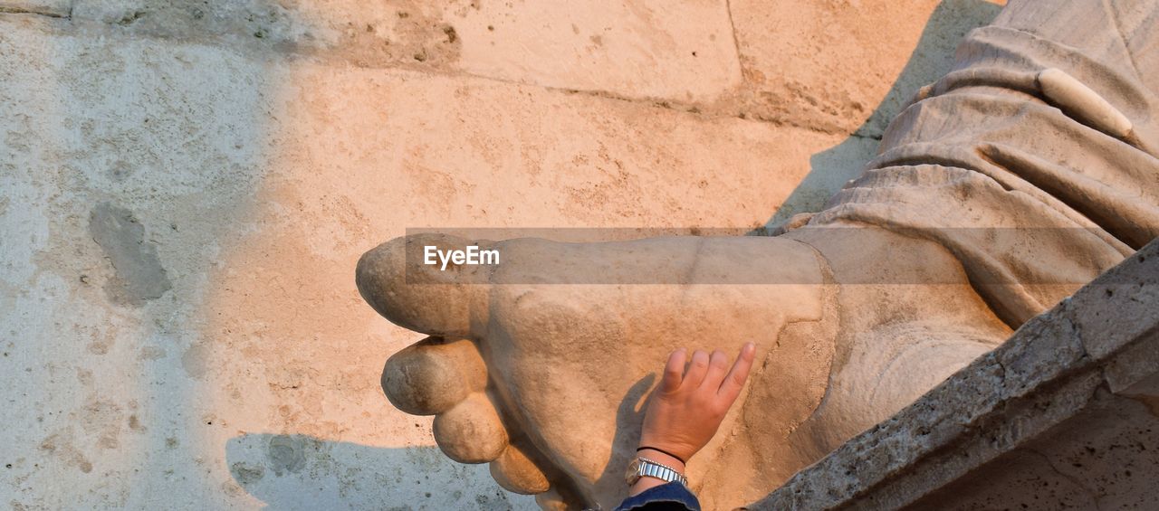 Cropped image of hand touching historic statue during sunset