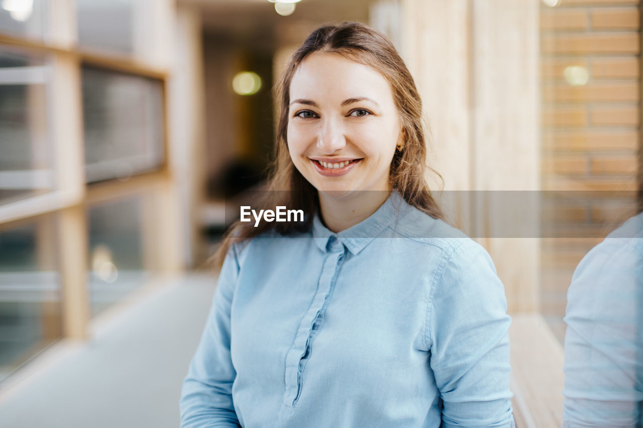 Portrait of happy young businesswoman standing at office corridor