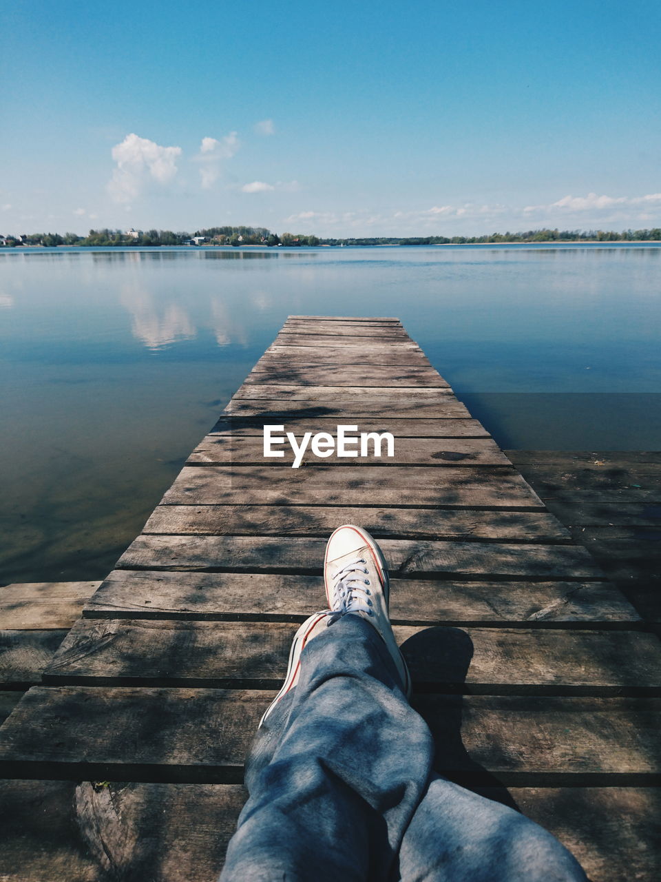 Low section of man lying on jetty in lake against sky