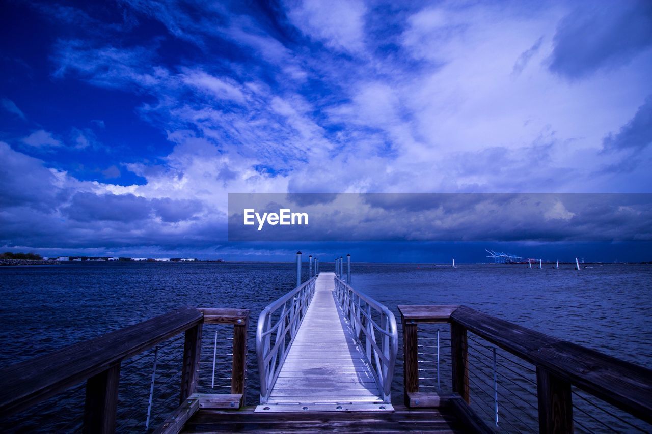 View of jetty leading to sea against cloudy sky