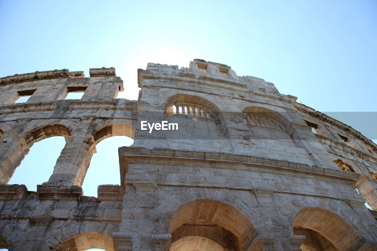 Low angle view of coliseum against clear blue sky