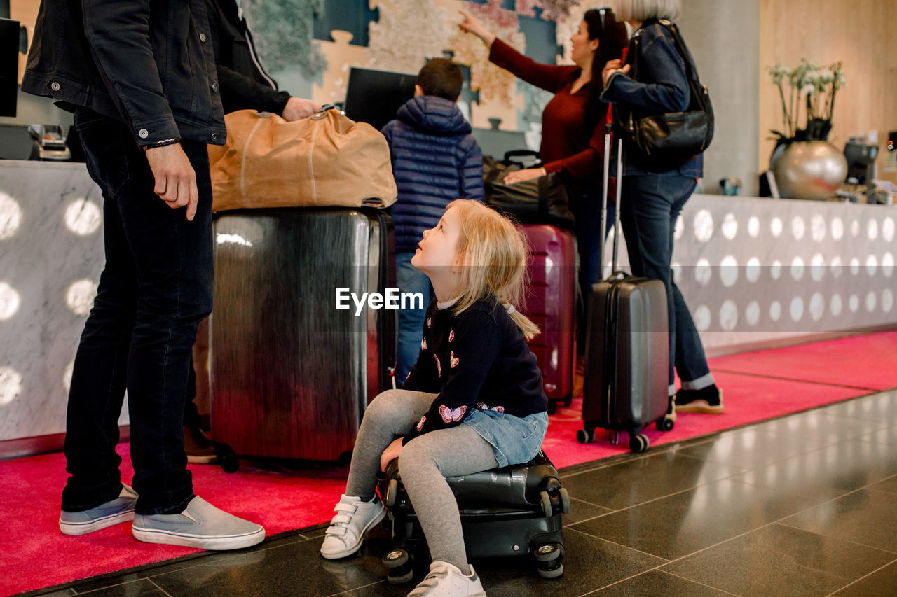 Girl sitting on suitcase while looking at father with family standing in background