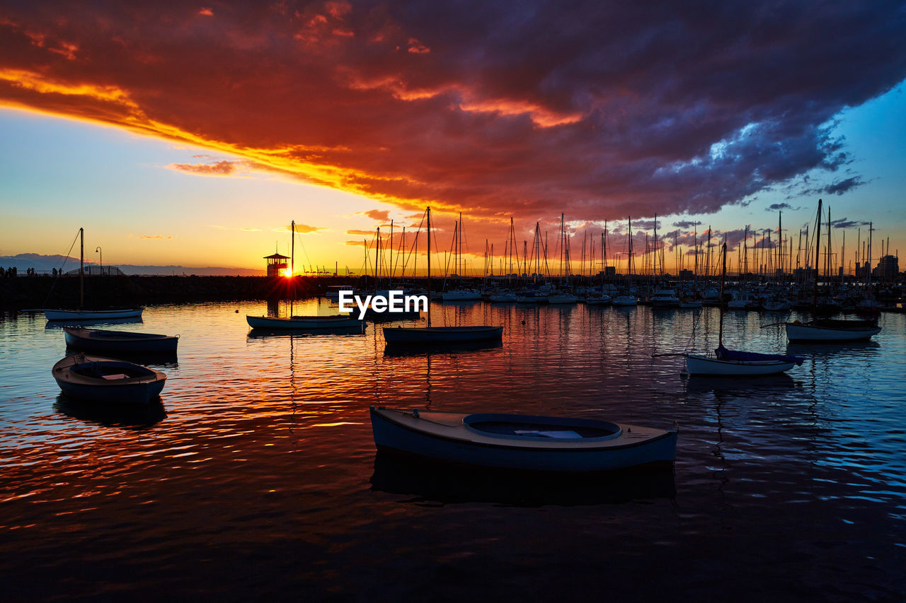 Sailboats moored in marina at sunset