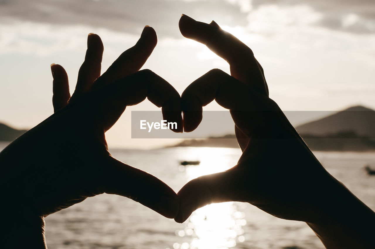 Heart shape with hand against sky during sunset