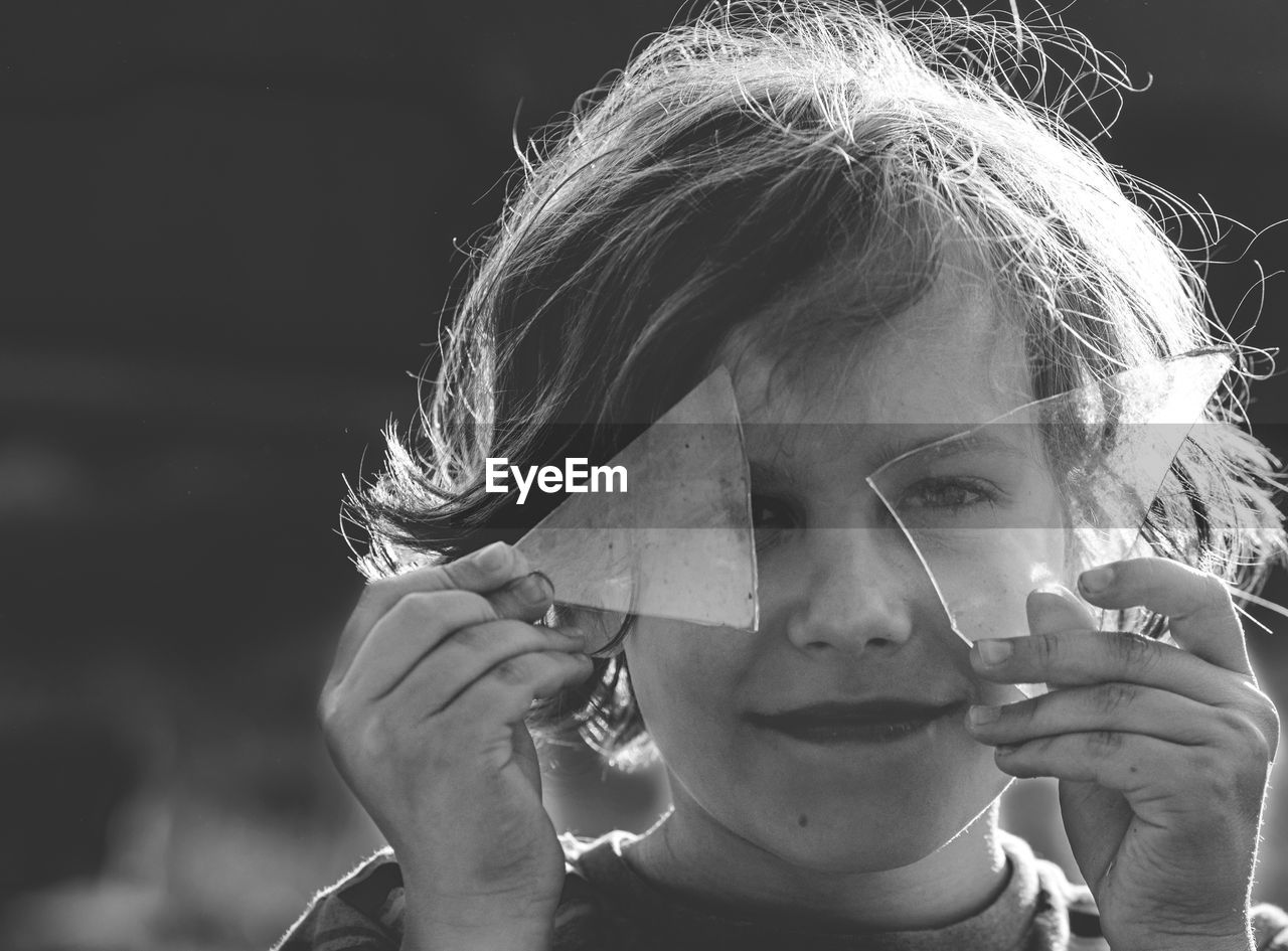 Portrait of boy holding broken glass over eyes