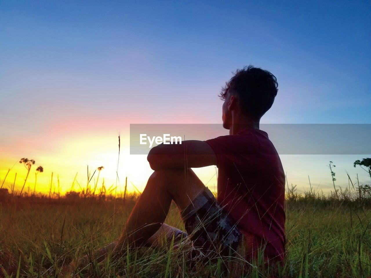 Side view of man sitting on field during sunset