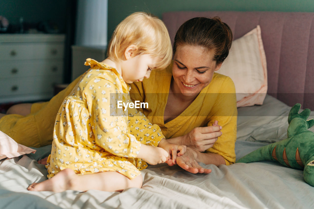 A little daughter playing with mother and paints her nails with polish.