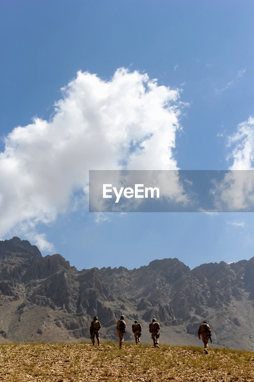 sky, mountain, cloud, landscape, environment, nature, mammal, mountain range, animal themes, animal, domestic animals, scenics - nature, land, group of people, group of animals, plateau, walking, beauty in nature, animal wildlife, travel, pet, leisure activity, wilderness, men, hiking, day, adult, horizon, outdoors, livestock, blue, travel destinations, activity, natural environment, non-urban scene, full length, rural scene, lifestyles
