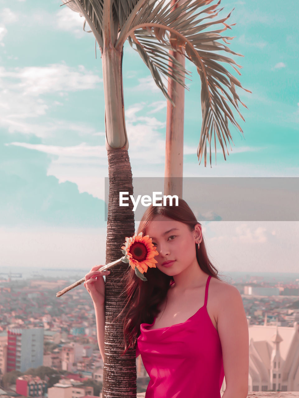 Portrait of girl standing by palm tree against sky
