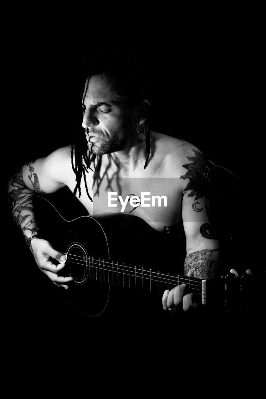 black and white, one person, musician, music, monochrome photography, adult, black background, arts culture and entertainment, musical instrument, guitar, studio shot, monochrome, string instrument, indoors, young adult, black, concert, darkness, musical equipment, portrait, performance, plucking an instrument, front view, lifestyles, person, copy space, tattoo, men