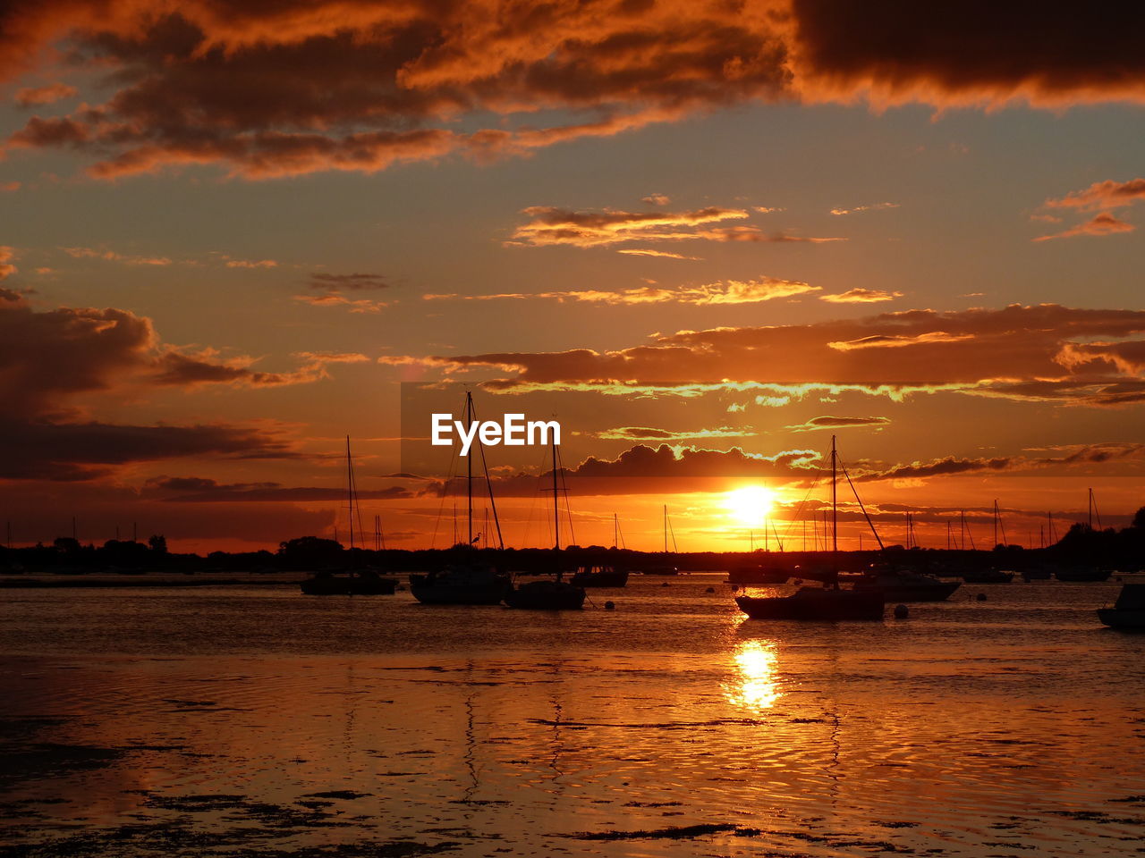 Silhouette sailboats moored on sea against sky during sunset