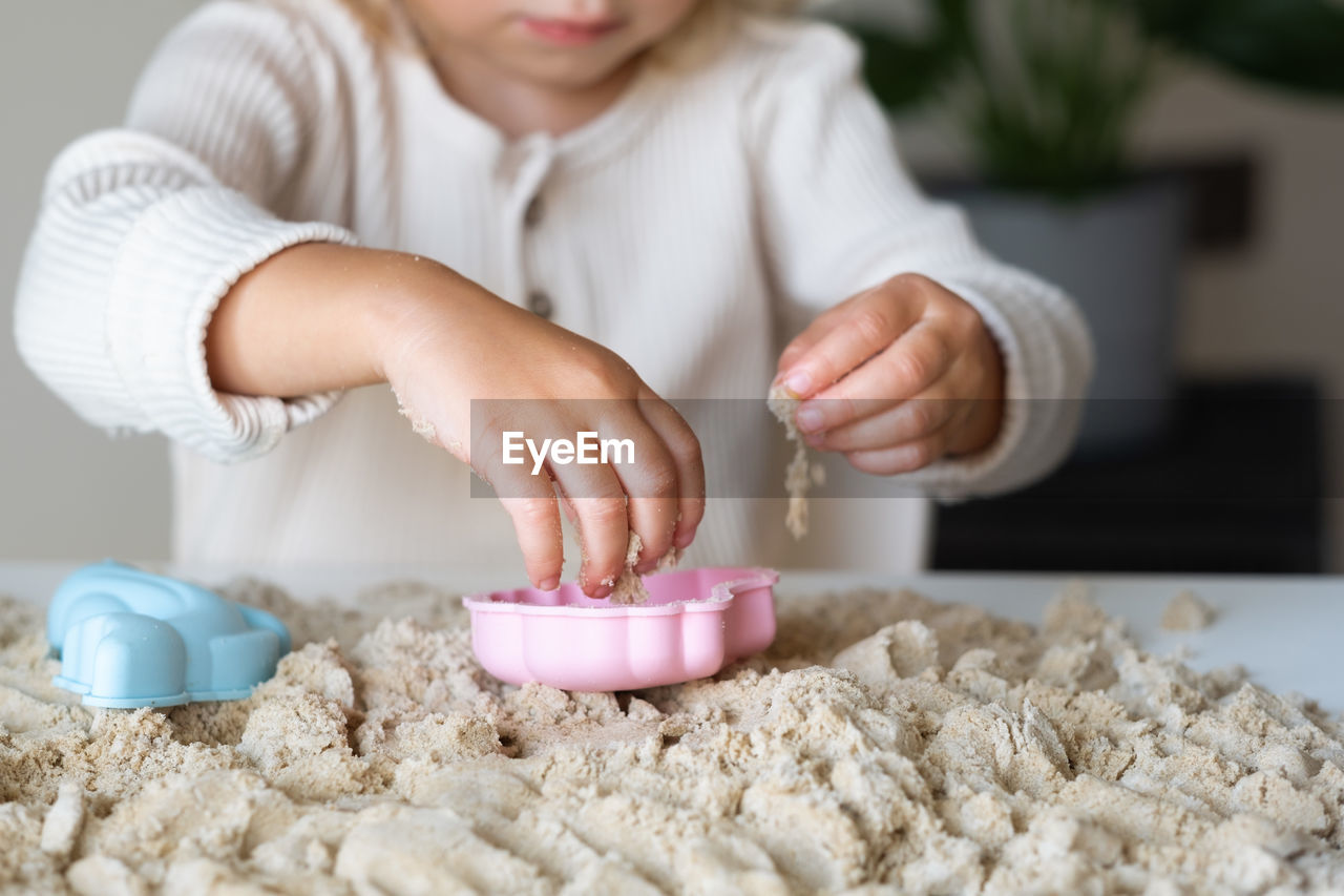 Blonde,curly-haired toddler,baby girl playing with kinetic sand indoors.motor skill, sensorics
