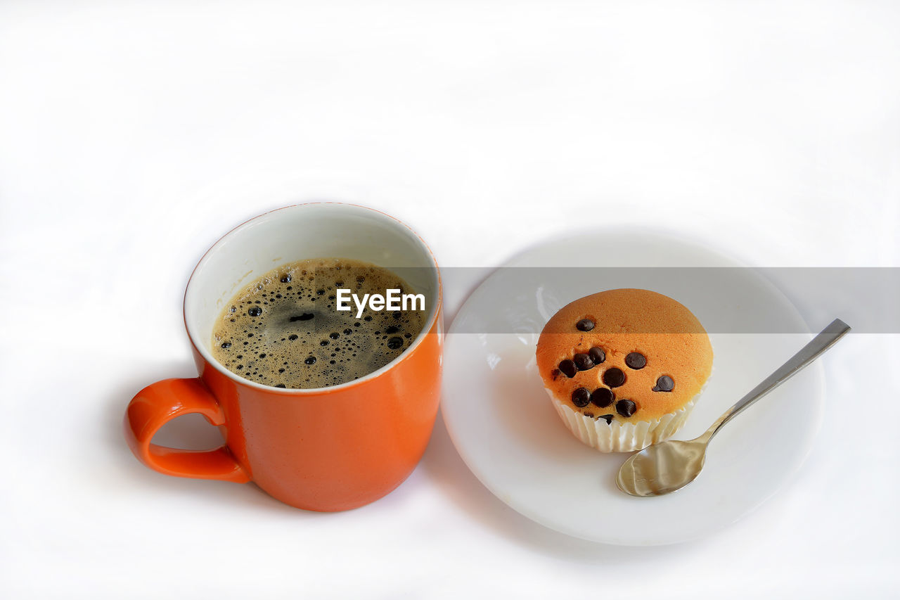 Close-up of coffee cup with muffin over white background